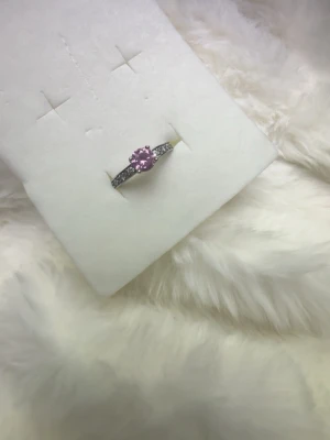 Silverring med rosa sten - Snygg silverfärgad ring med en rund, rosa sten i mitten och små klara stenar längs bandet. Ringen har en klassisk design med gnistrande detaljer som verkligen fångar ögat. Perfekt för dig som vill ha något unikt och stilrent.