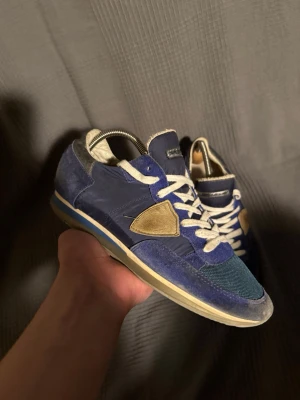 Philippe Model - Snygga blå sneakers från Philippe Model med vita skosnören och beige detalj på sidan. Skorna har en mix av mocka och textilmaterial, samt en kontrasterande blå och beige sula. Perfekta för dig som gillar en sportig och trendig look.