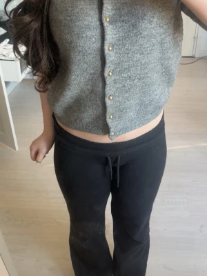 Grå kortärmad kofta med pärlknappar - Säljer en grå, mjuk och stickad kofta med korta ärmar och pärlknappar framtill. Koftan har en croppad passform och ribbade kanter vid ärmslut och nederkant. Perfekt för lager på lager och enkel att styla till olika outfits.