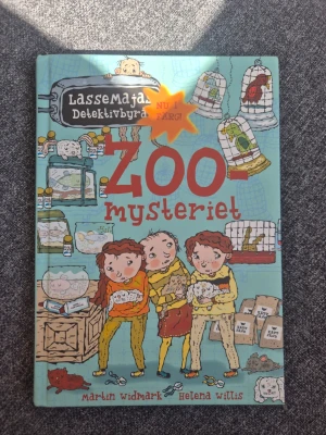Zoo-mysteriet LasseMajas Detektivbyrå - En färgglad och illustrerad barnbok med titeln 'Zoo-mysteriet' från serien LasseMajas Detektivbyrå. Boken har hårda pärmar i blått med tecknade figurer och djur på omslaget. Perfekt för dig som gillar mysterier och spännande äventyr.