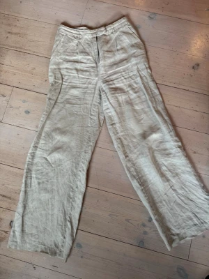 Beige vida linnebyxor - Säljer ett par beige linnebyxor med hög midja och vida ben. Byxorna har klassisk dragkedja fram och fickor i sidorna. Perfekta för en avslappnad och trendig look. Materialet är 100% linne vilket gör dem svala och sköna.