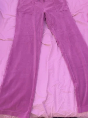 Lila mjukisbyxor i velour - Säljer ett par rosa mjukisbyxor i mjuk velour Byxorna har fickor fram och två bakfickor med lock och knapp. Har använt max 3 gånger 
