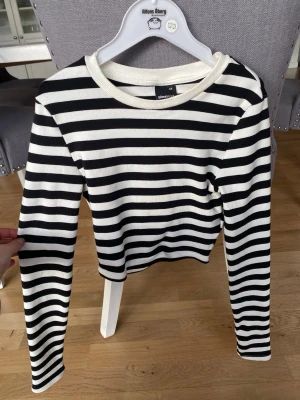 Randig långärmad tröja Gina Tricot - Snygg långärmad tröja från Gina Tricot i svart och vitt med klassiskt horisontellt randigt mönster. Tröjan har rund halsringning och är tillverkad i mjukt, stretchigt material som sitter skönt på kroppen. Perfekt för en trendig och avslappnad look. Köparen står för frakt.