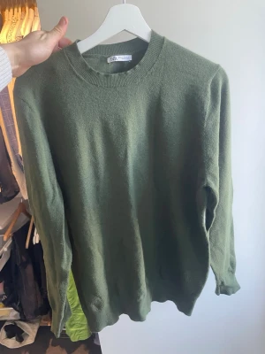 Olivgrön stickad tröja från Zara - Snygg olivgrön stickad tröja från Zara med rund halsringning och ribbade muddar. Tröjan har en enkel och clean design som passar perfekt till jeans eller kjol. Materialet känns mjukt och skönt mot huden. Perfekt för lager på lager under kyliga dagar.