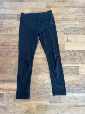 Svarta leggings från Hummel - Snygga svarta leggings från Hummel med diskret logga på höften. De har en hög midja och är tillverkade i ett stretchigt material som sitter skönt mot kroppen. Perfekta för träning eller chill dagar.