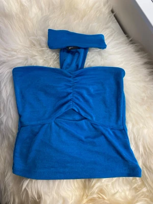 Blå bandeau tubtopp med scrunch - Snygg blå bandeau tubtopp med scrunch-detalj framtill. Toppen är ärmlös och har en tight passform, perfekt för sommaren. Tillverkad i mjukt bomullsmaterial som känns skönt mot huden. Enkel men trendig design som sticker ut.