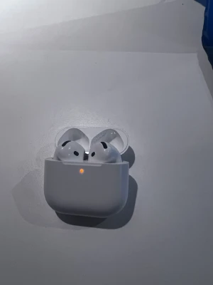Trådlösa vita hörlurar Apple AirPods - Säljer ett par stilrena vita Apple AirPods med laddningsetui. Hörlurarna är kompakta, har en smidig form och laddas enkelt i det medföljande etuiet. Perfekta för musik, poddar och samtal på språng.