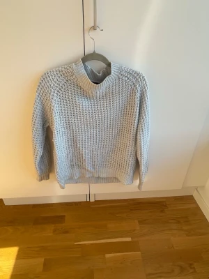 Ljusgrå chunky stickad tröja - Säljer en ljusgrå chunky stickad tröja med grov struktur och rund hals. Tröjan har långa ärmar och ribbade muddar vid ärmslut och nederkant. Perfekt för kalla dagar och enkel att styla till olika outfits.