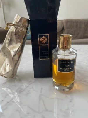 Mancera Tonka Cola Eau de Parfum - Mancera Tonka Cola Eau de Parfum i elegant glasflaska med guldfärgat lock. Kommer med svart och guld kartong samt en lyxig guldfärgad tygpåse med dragsko. Doften har en varm, kryddig och söt tonka- och koladoft. Perfekt för dig som gillar unika och exklusiva parfymer. Har använt en del, är ca ett och ett halvt år gammal. 
