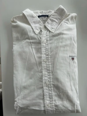 Vit skjorta från Gant - Klassisk vit skjorta från Gant med button-down krage och lång ärm. Skjortan har broderad logga på bröstet och knäppning framtill. Tillverkad i bomull för en skön och stilren känsla. Perfekt till jeans eller chinos för en clean look.