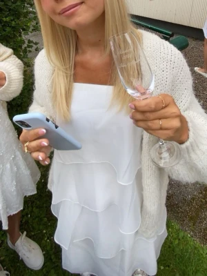 Vit volangklänning med tunna axelband - Säljer en superfin vit kortklänning med flera lager volanger och tunna axelband som knyts på axlarna. Klänningen har en luftig och flowy passform, perfekt för varma dagar. Materialet känns lätt och svalt, vilket gör den extra bekväm. Använd en gång, perfekt för studenten eller sommaren ☀️😍🥂