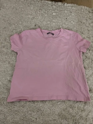 Ljusrosa t-shirt från Zara - En enkel och stilren ljusrosa t-shirt från Zara. T-shirten har rund halsringning och korta ärmar. Tillverkad i mjuk bomull som känns skön mot huden. Perfekt basplagg att matcha med allt.