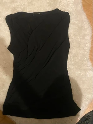 Svart omlottopp från Anna Field - Säljer en svart omlottopp från Anna Field. Toppen är ärmlös och har en snygg omlottdesign framtill som ger en stilren look. Materialet känns mjukt och stretchigt, troligen polyester eller bomullsmix. 