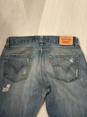 Levi's 512 Bootcut ljusblå jeans med sjuk tvätt - Säljer ett par klassiska Levi's 512 Bootcut jeans i ljusblå tvätt. Jeansen har slitna detaljer, fem fickor och den ikoniska röda Levi's-lappen på bakfickan. Perfekt för dig som gillar en avslappnad och tidlös stil. Mått: midja 44-45cm, längd 113cm, benöppning 22-23cm 
