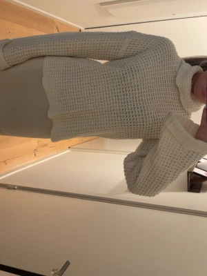 Vit stickad polotröja - Mysig vit stickad polotröja med grovstickat mönster och långa ärmar. Tröjan har en hög polokrage och avslappnad passform, perfekt för kyliga dagar. Passar till både jeans och kjol för en enkel och stilren look.