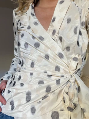 Prickig omlottblus  - Superfin och unik omlottblus med beiga och svarta prickar. Blusen har knyt i midjan, v-ringning och långa ärmar. Köpt secondhand men i perfekt skick💗💗