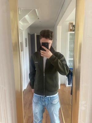 Zip hoodie från Les Deux  - Snygg mörkgrön hoodie från Les Deux med dragkedja framtill och hög krage. Tillverkad i mjukt material och har ribbade muddar vid ärmslut och nederkant. Perfekt för en avslappnad och stilren look. Storlek M men kan kännas som S i längden. Tveka inte att skriva vid intresse 😉✍️