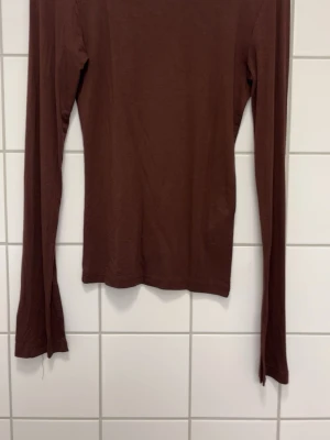 Brun långärmad topp - En enkel och stilren brun långärmad topp med rund hals. Modellen är figurnära och passar perfekt till både jeans och kjol. Tillverkad i mjukt material som känns skönt mot huden. Perfekt basplagg för garderoben.