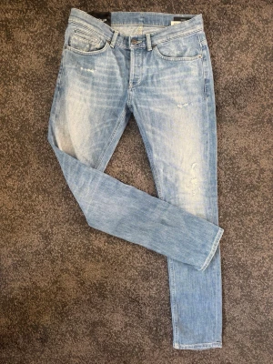 Dondup Jeans - Säljer ett par ljusblå skinny jeans från Dondup med slitna detaljer och klassisk femficksmodell. Jeansen har en snygg tvätt och Dondup-logga bak i midjan. Perfekta för dig som gillar en avslappnad men trendig stil.