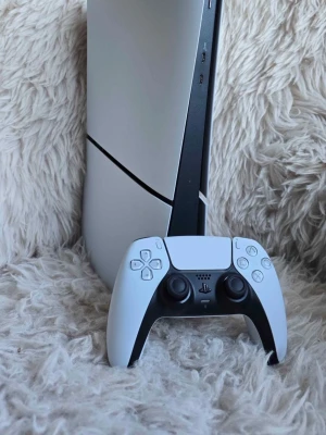 Sony PlayStation 5 Digital Edition - Säljer en Sony PlayStation 5 Digital Edition med en vit och svart DualSense-kontroll. Konsolen har en futuristisk design med rundade kanter och matta ytor i plast. Perfekt för gaming i 4K och HDR, och levereras med originalkartong.