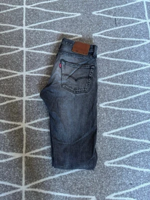 Grå Levi's 501 jeans - Säljer ett par klassiska grå Levi's 501 jeans med rak passform och femficksmodell. Jeansen har en snygg tvättad look, ikonisk röd Levi's-tag på bakfickan och läderpatch i midjan. Tillverkade i slitstark bomull, perfekta för en avslappnad stil. Storlek W28 L32. Hör av er vid frågor eller lägg ett prisförslag!
