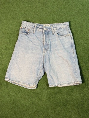 Ljusblå denimshorts från Jack & Jones - Klassiska ljusblå denimshorts från Jack & Jones med fem fickor och normal passform. Shortsen har bälteshällor, knappgylf och raka ben. Perfekta för varma dagar och enkel att matcha med olika stilar.
