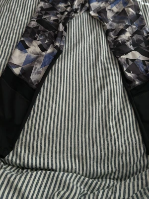 Mönstrade leggings med meshdetaljer - Säljer ett par leggings med svart, blått och vitt geometriskt mönster upptill och svarta meshpaneler nedtill på benen. Stretchigt material som sitter tight och är perfekta för träning eller en sportig look.