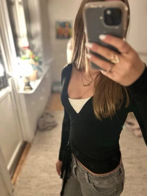 Svart omlottopp med snörning - Säljer snygg svart omlottopp med v-ringning och långa ärmar. 