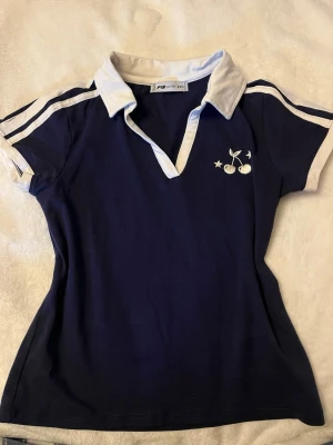 Marinblå kortärmad topp FB Sister - Sportig marinblå topp från FB Sister med vita detaljer, korta ärmar och krage.