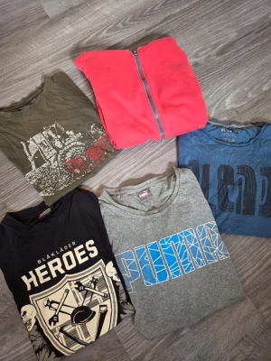Klädpaket Herr - Klädpaket med 5 tröjor.  - Grå Puma t-shirt, litet hål men syns inte vid användning. - Blå t-shirt från Blend. - Svart t-shirt från Blåkläder - Grön t-shirt från Bluewear. - Röd hoodie med dragkedja från Cubus, nopprig och någon fläck på ärmarna, vet ej om det går bort i tvätten, har inte testat.  Vissa plagg har lätt slitage/fläck (se bilder) men fortfarande fina och fullt användbara. Säljs som klädpaket. Bundle 50% fri frakt  bundle50% bundle50 frifrakt