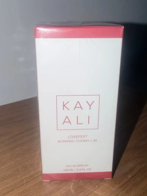 Kayali Lovefest Burning Cherry 48 EdP - Kayali Lovefest Burning Cherry 48 Eau de Parfum är en parfym i en stilren vit och röd förpackning. Doften kommer i en 100 ml flaska och har en modern, minimalistisk design med röda detaljer. Perfekt för dig som gillar fruktiga och unika doftnoter.