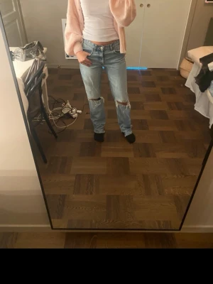 Ljusblå ripped jeans med raka ben - Säljer ett par ljusblå jeans med raka ben och slitna hål på båda knäna. Jeansen har klassisk femficksdesign och normal midja. Har själv klippt en slits längst ner för att få den mer rak i modellen