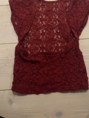 Bordeaux spetsblus med kort ärm - Snygg bordeauxfärgad blus i spets med korta ärmar. Blusen är genombruten med blommigt spetsmönster och har en feminin, figurnära passform. Perfekt att styla med jeans eller kjol för en trendig look.