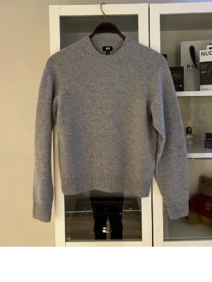 Grå stickad tröja från Uniqlo - En stilren grå stickad tröja från Uniqlo med rund halsringning och ribbade muddar vid ärmslut och nederkant. Perfekt för lager-på-lager och enkel att matcha med olika outfits. Materialet ser ut att vara mjukt och bekvämt. Helt oanvänd. Perfekt skick och riktigt go. Skriv vid fundering!
