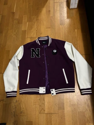 Varsity jacka - Lila och Vit  - Stilren varsity-jacka med unikt tryck både fram och bak. Trendig lila och vit  färgkombination med detaljer som sticker ut. Storlek L, normal passform. Helt ny/knappt använd och i perfekt skick – redo att användas direkt!