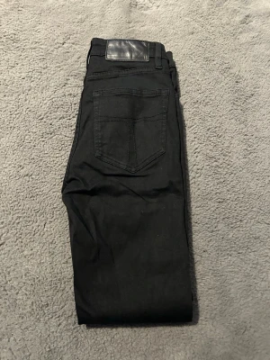 Svarta jeans från Jack & Jones - Snygga svarta jeans från Jack & Jones med klassisk femficksdesign och svart läderpatch bak i midjan. Jeansen har raka ben och är tillverkade i ett mjukt bomullsmaterial med lite stretch för extra komfort.