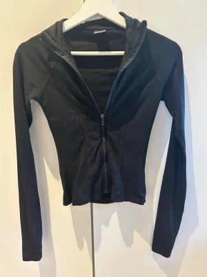 Svart zip hoodie från Gina Tricot - Säljer en svart hoodie från Gina Tricot med dragkedja framtill och åtsittande passform. Hoodien har långa ärmar och är tillverkad i ett mjukt bomullsmaterial. Perfekt för en avslappnad och stilren look.