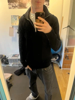 Svart stickad tröja med dragkedja - Säljer en svart stickad tröja från Arket med hög krage och dragkedja framtill. Tröjan har ribbad struktur, långa ärmar och en avslappnad passform. Perfekt för lager på lager och enkel att matcha med olika outfits.