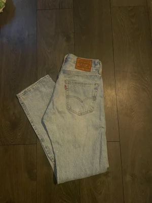 Levi's ljusblå raka jeans - Klassiska ljusblå jeans från Levi's med rak passform och hög midja. Jeansen har fem fickor, Levi's ikoniska läderpatch bak och röd etikett på bakfickan. Tillverkade i slitstark denim, perfekta för en avslappnad och trendig look.