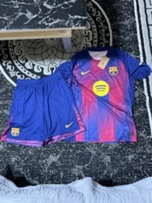 FC Barcelona matchställ Nike med shorts - Säljer ett FC Barcelona matchställ från Nike med Dri-Fit material. Tröjan har blå och röda vertikala ränder, klubbmärke och sponsorlogga på bröstet samt Nike-logga. Tillhörande shorts i blått med klubbmärke och Nike-logga. Perfekt för fotbollsträning.