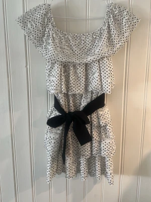 Prickig volangklänning från Zara - Supersöt kort klänning från Zara i vitt med svarta prickar, volangdetaljer och en stor svart rosett i midjan. 