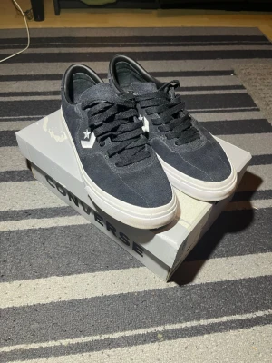 Svarta Converse CONS One Star sneakers - Snygga svarta Converse CONS One Star sneakers i mocka med vita detaljer och vit sula. Klassisk låg modell med svart snörning och stjärnlogga på sidan. Perfekta för dig som gillar streetwear och skatevibe.