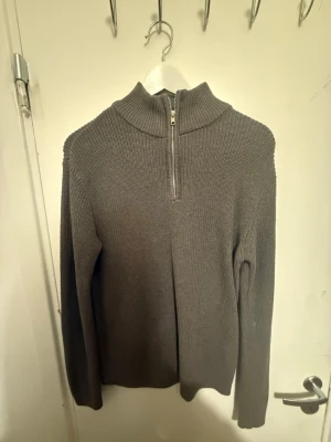 Brun  stickad tröja med halv dragkedja - Mysig brun  stickad tröja med hög krage och halv dragkedja framtill. Tröjan har lång ärm och är ribbstickad för en stilren look. Perfekt för lager på lager och enkel att matcha med olika outfits. Finns S,M,L i storlek 