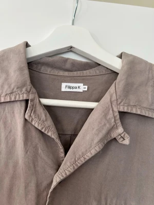 Beige kortärmad skjorta Filippa K - Stilren beige skjorta från Filippa K med korta ärmar och klassisk krage. Skjortan har knappar framtill och en bröstficka. Tillverkad i mjuk bomull som känns skön mot huden. Perfekt för en avslappnad och trendig look. Använd endast vid ett tillfälle, annars precis som ny! Ny pris ligger runt 1500-1800, Så om du vill passa på o fynda, titta inte längre, pris går att diskutera;)