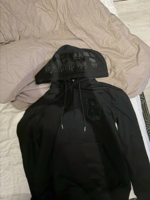 Svart hoodie från Risky med tryck - Svart hoodie från Risky med huva och dragsnören. På huvan finns ett svart tryck med droppande effekt och på bröstet sitter en svart patch i form av ett R. Hoodien har en klassisk känguruficka och är gjord i mjukt bomullsmaterial priset är inte hugget i sten så kom med bud😊.