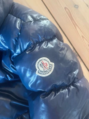 Blå Moncler jacka  - Snygg blå dunjacka från Moncler med glansigt material och klassisk logga på ärmen. Jackan är i storlek 4 vilket passar xs-m äkthetsbevis i jackan.