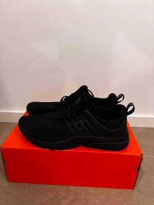 Svarta Nike Air Presto sneakers - Svarta Nike Air Presto sneakers med låg profil och sportig design. Skorna har en ovandel i mesh och syntet, elastiska snören och en bekväm sula. Perfekta för en stilren och clean look. Sitter skönt på foten och har diskret Nike-logga på innersulan.