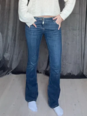Blå bootcut jeans med låg midja - Snygga blå bootcut jeans med låg midja och klassisk femficksmodell. Jeansen har en lätt tvättad look och stängs med dragkedja och knapp. Perfekta för dig som gillar en avslappnad men trendig stil.
