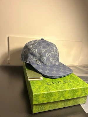 Blå denimkeps från Gucci - Snygg blå keps från Gucci i denim med klassiskt GG-monogram över hela kepsen. Böjd skärm och justerbar baksida. Perfekt accessoar för att lyfta din streetwear-look med exklusiv känsla.