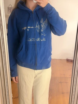 Blå hoodie med tryck och dragkedja - Blå hoodie med dragkedja och huva, dekorerad med ett glittrigt tryck